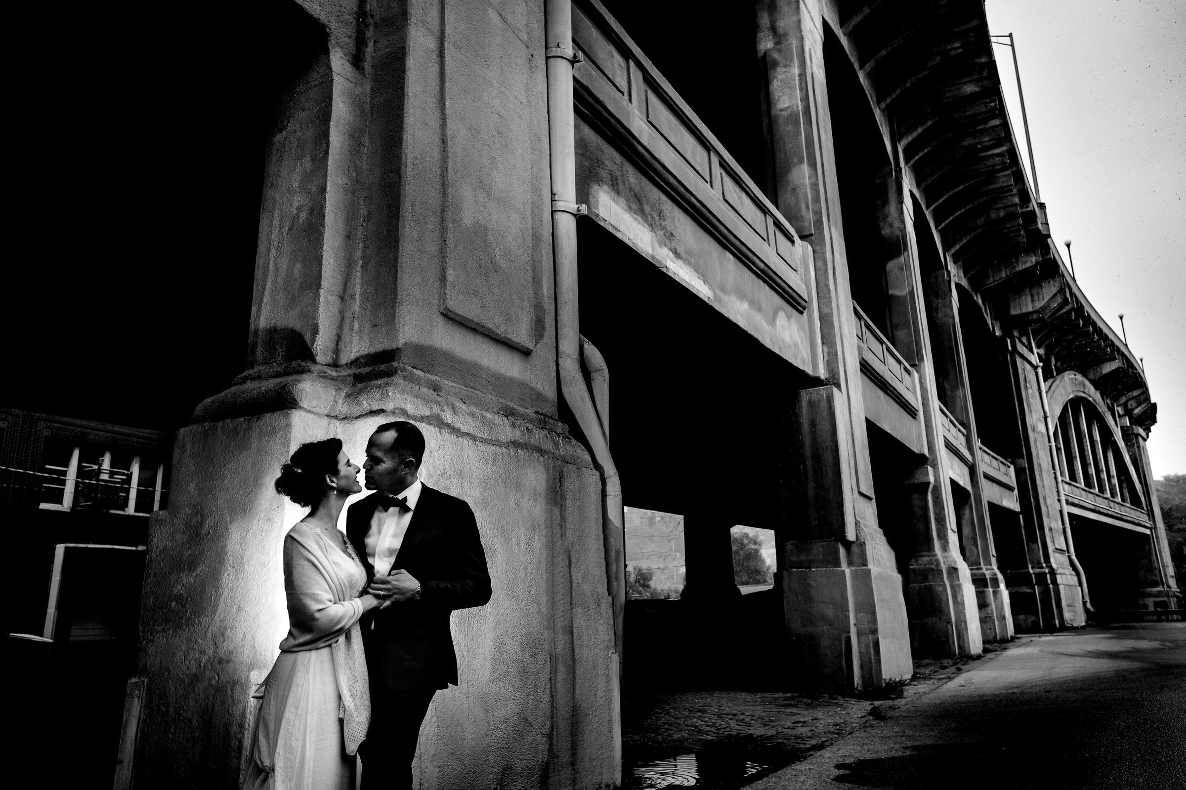 Bride and groom lit with off-camera flash beneath a concrete bridge during a wedding portrait